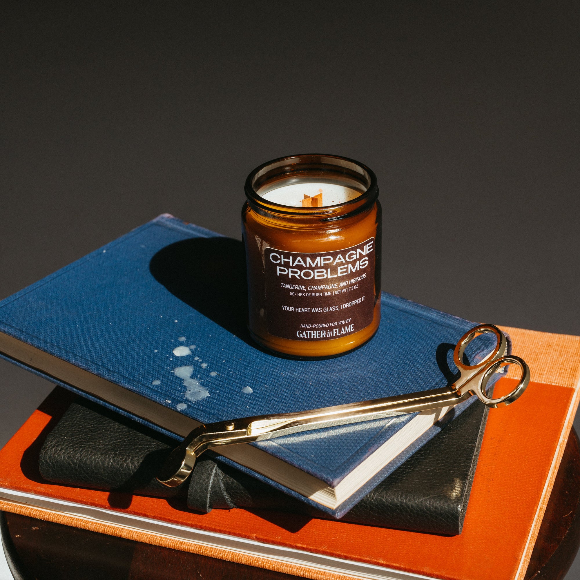 Candle labeled 'Champagne Problems' on a stack of books with a pair of scissors.