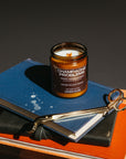 Candle labeled 'Champagne Problems' on a stack of books with a pair of scissors.