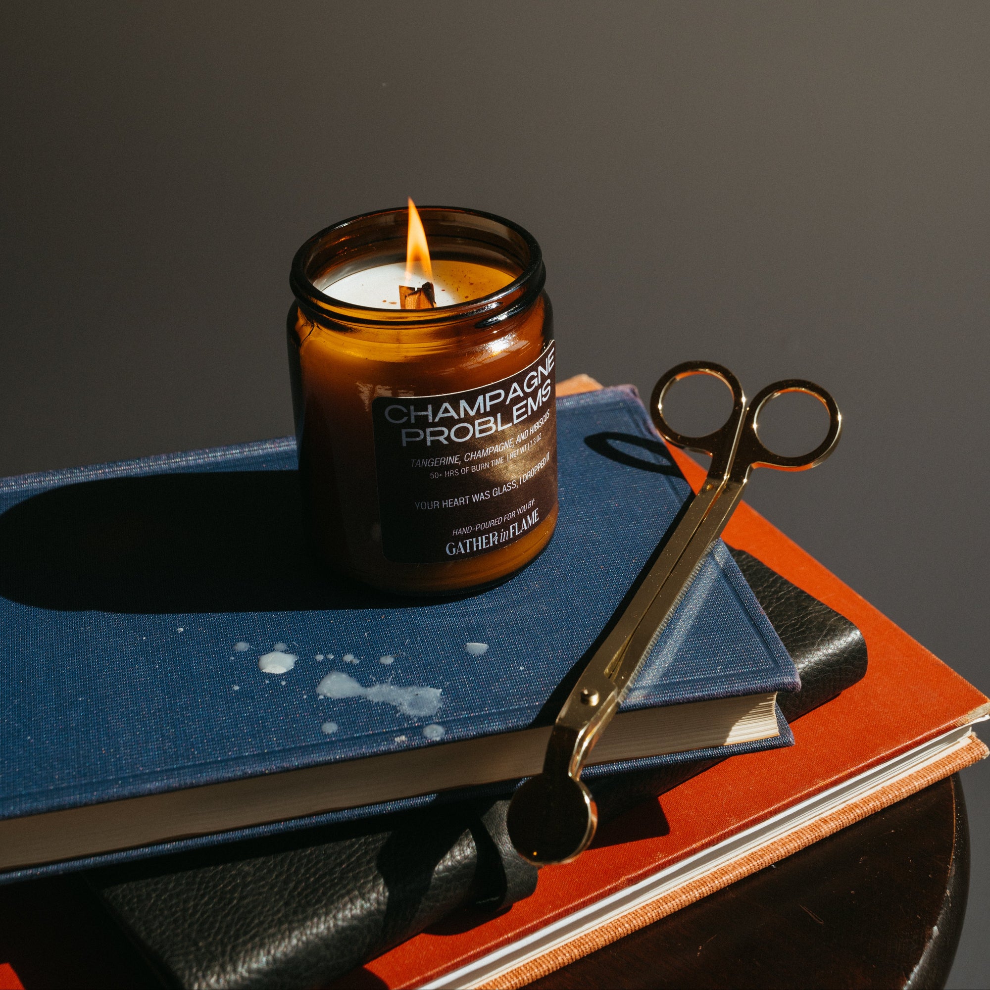 Candle in a brown glass jar on a book with a pair of scissors next to it against a dark background