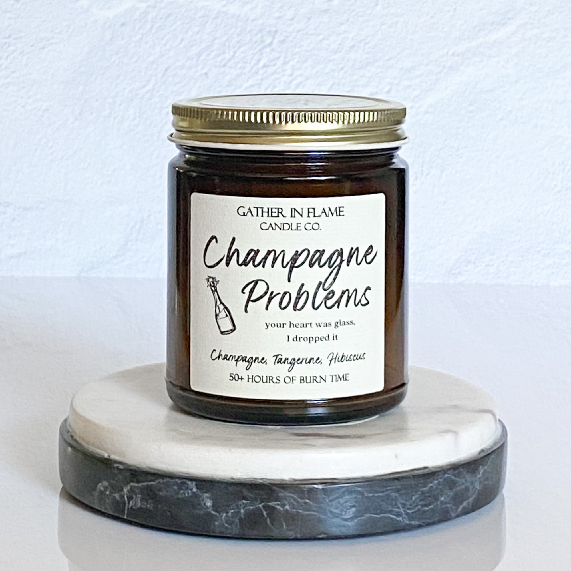 A jar candle with a label reading 'Champagne Problems' and topped with multi-colored eco-glitter, sitting on a marble surface.