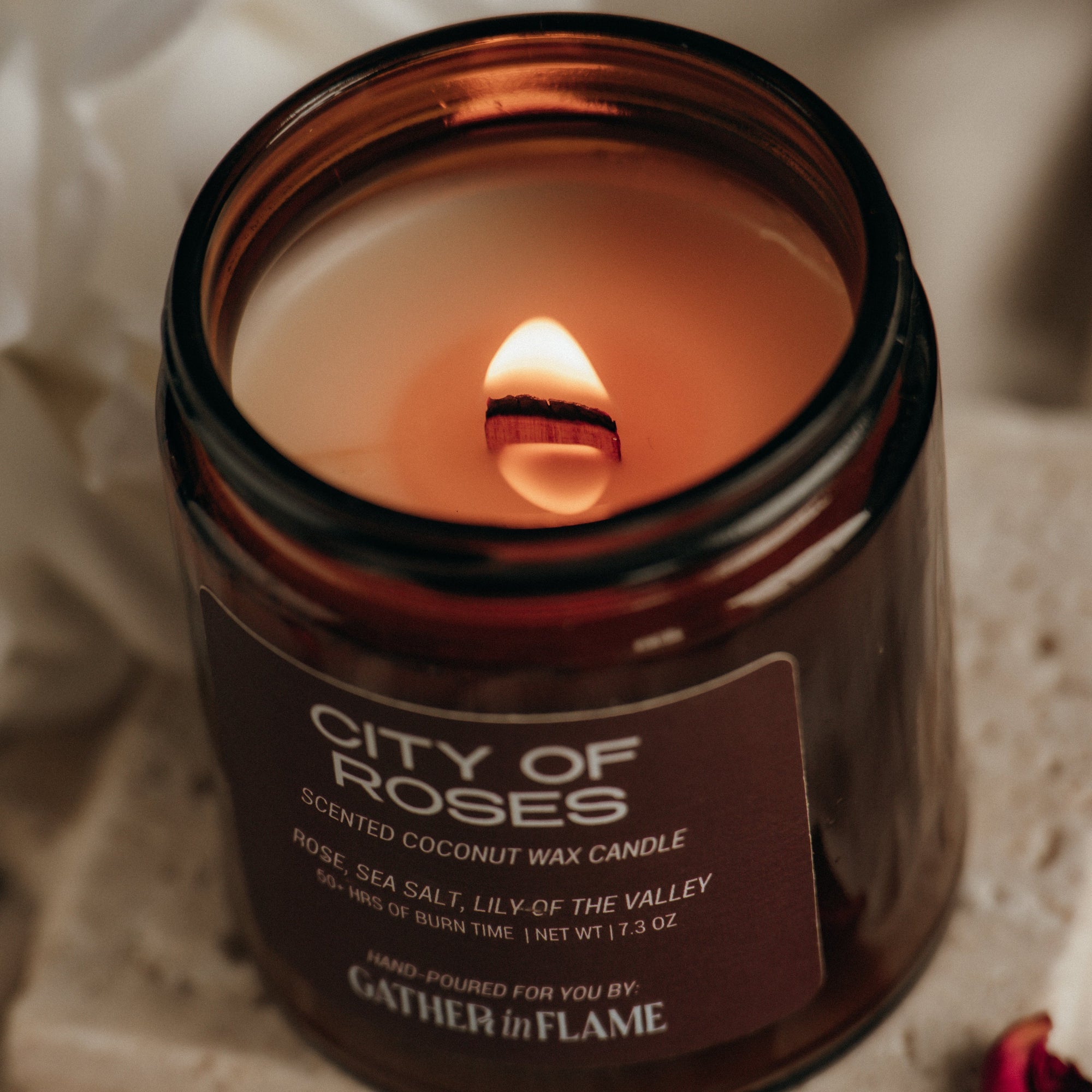 Candle labeled 'City of Roses' by 'Flame' on a textured surface.