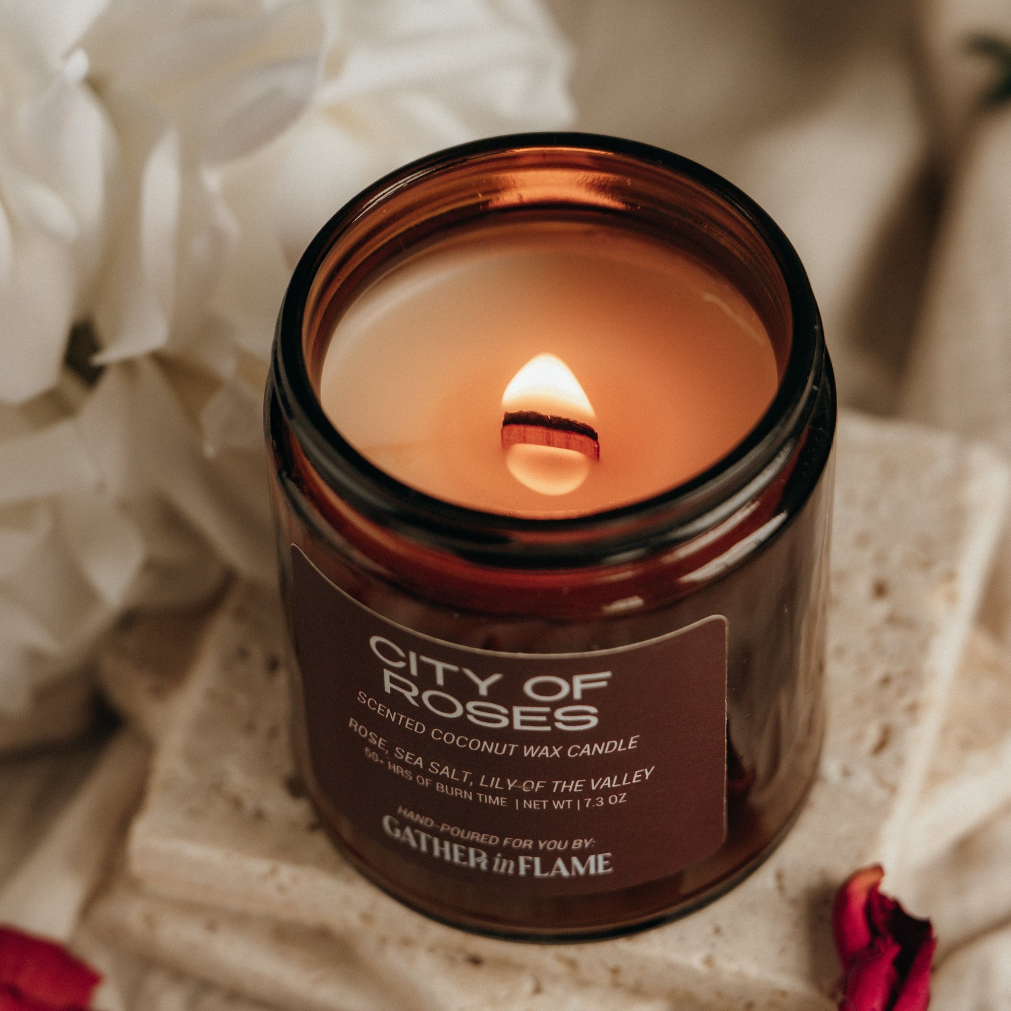 Candle in a brown jar labeled 'City of Roses' with white flowers in the background