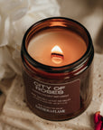 Candle in a brown jar labeled 'City of Roses' with white flowers in the background
