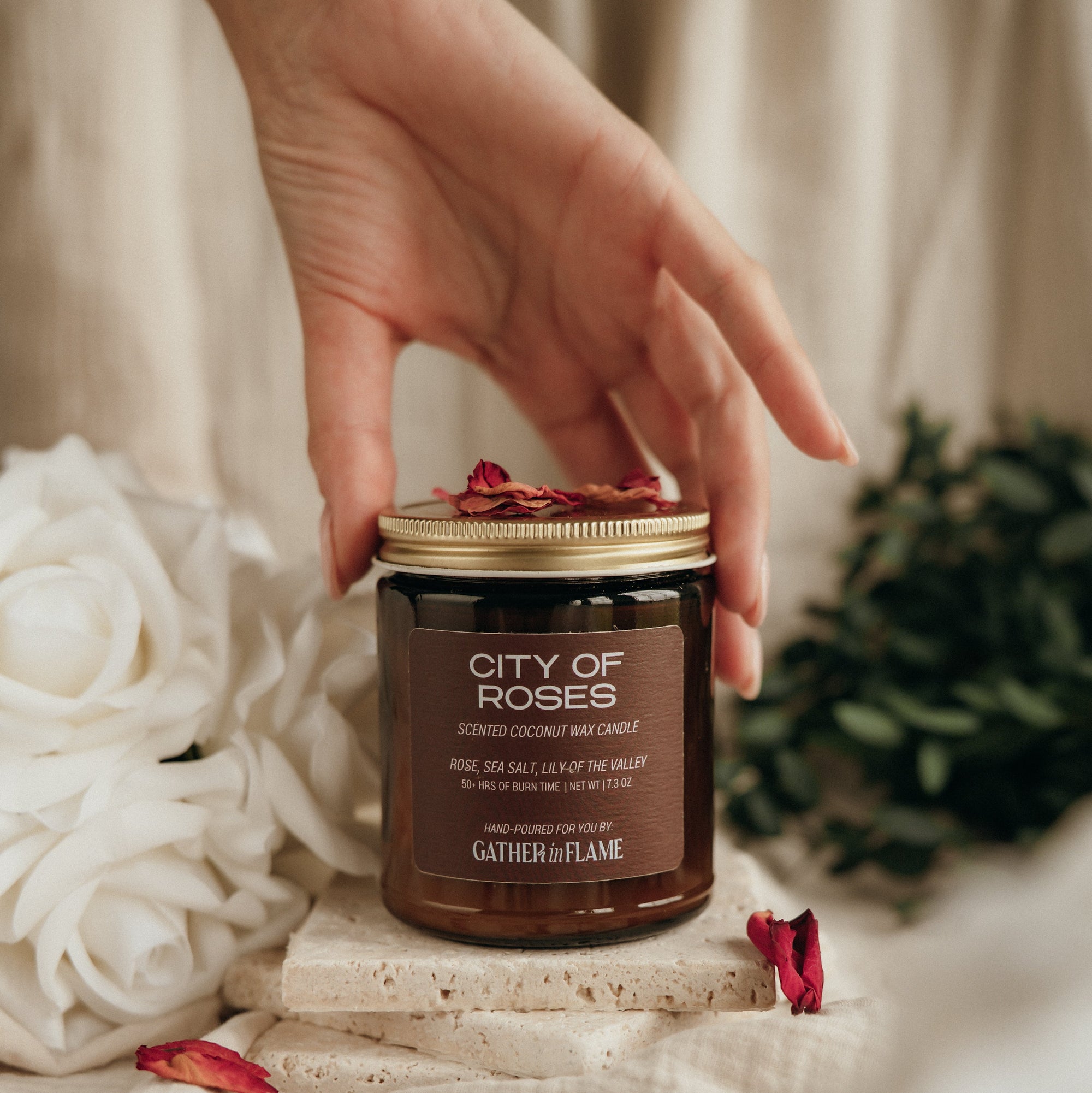 Hand holding a 'City of Roses' candle with decorative elements on a soft background