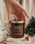 Hand holding a 'City of Roses' candle with decorative elements on a soft background