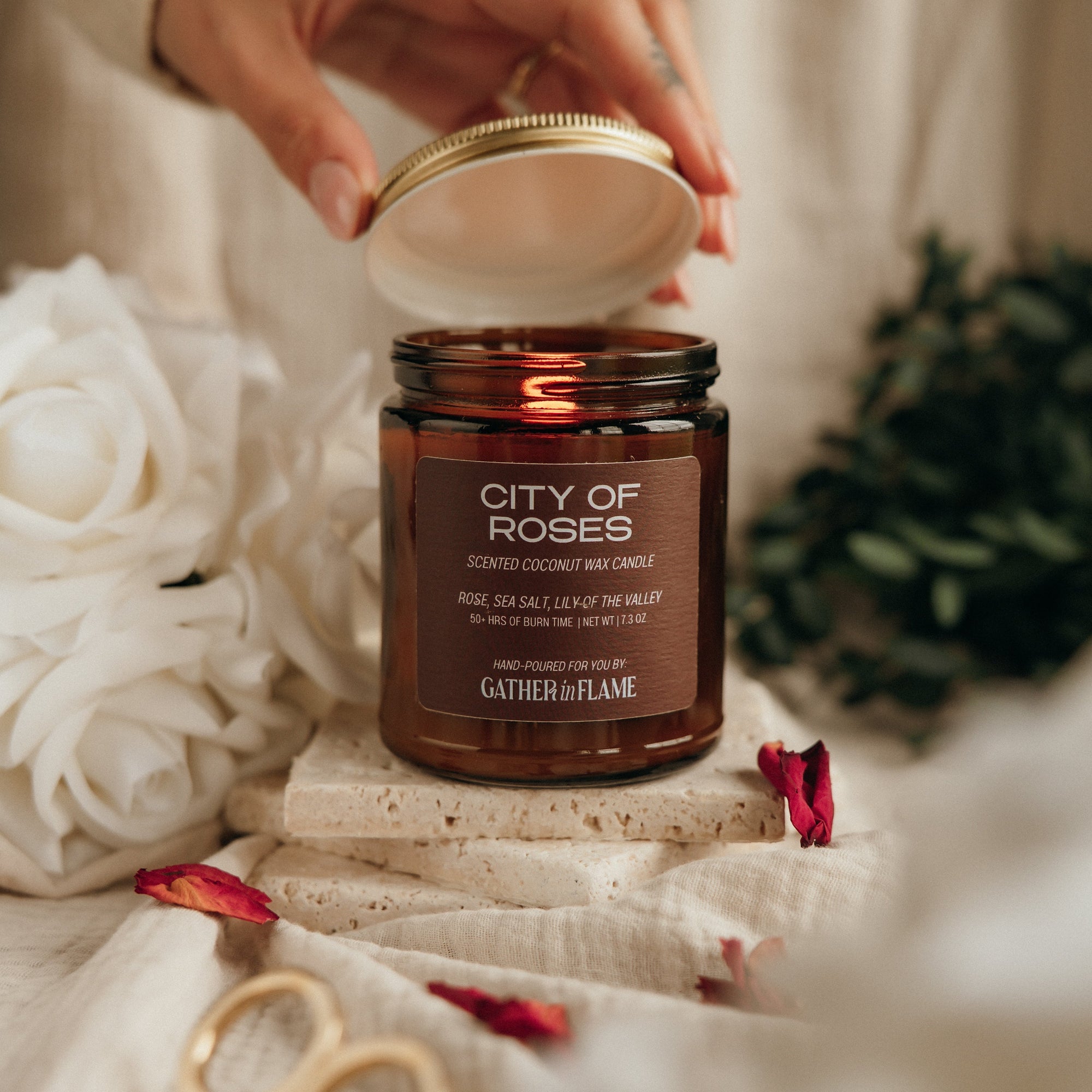 Hand holding a jar of 'City of Roses' candle with decorative elements on a soft background