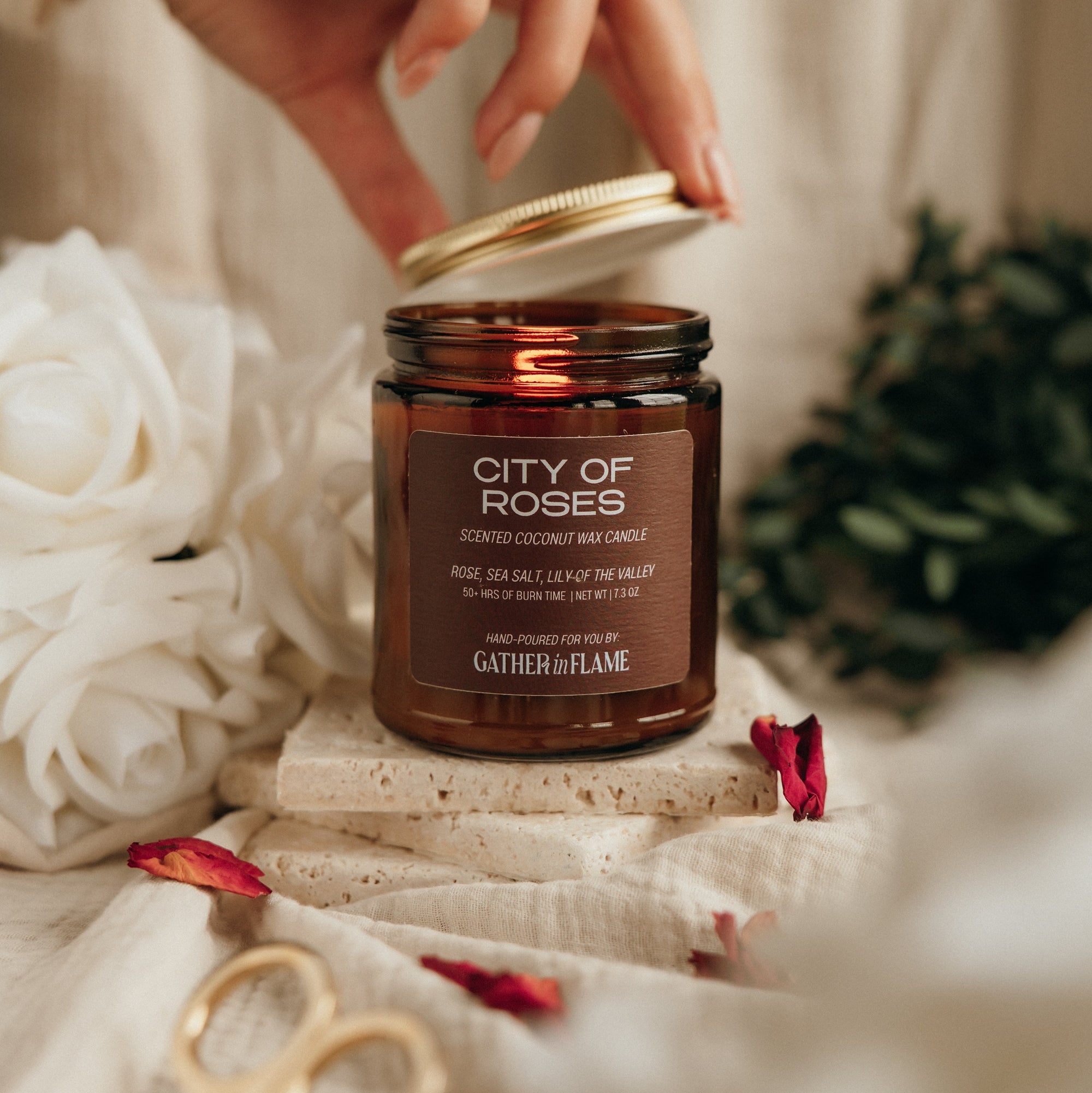Candle jar labeled 'City of Roses' being held by a hand with decorative elements around it.