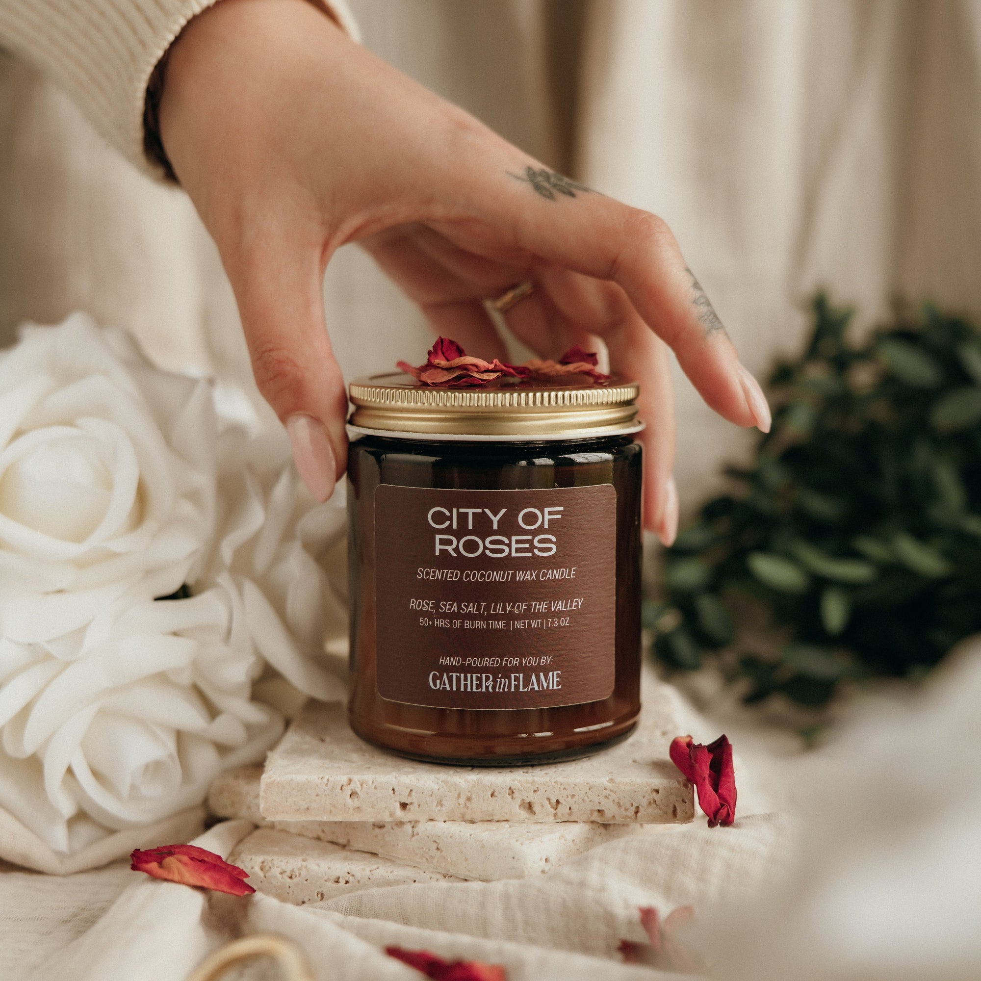 Hand holding a 'City of Roses' candle with decorative elements on a soft background