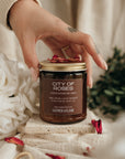 Hand holding a 'City of Roses' candle with decorative elements on a soft background