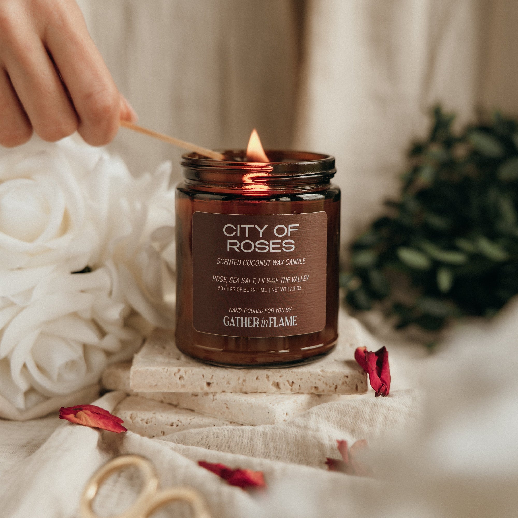 Candle labeled 'City of Roses' being lit with a wooden match, surrounded by flowers and decorative items.
