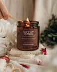 Candle labeled 'City of Roses' being lit with a wooden match, surrounded by flowers and decorative items.