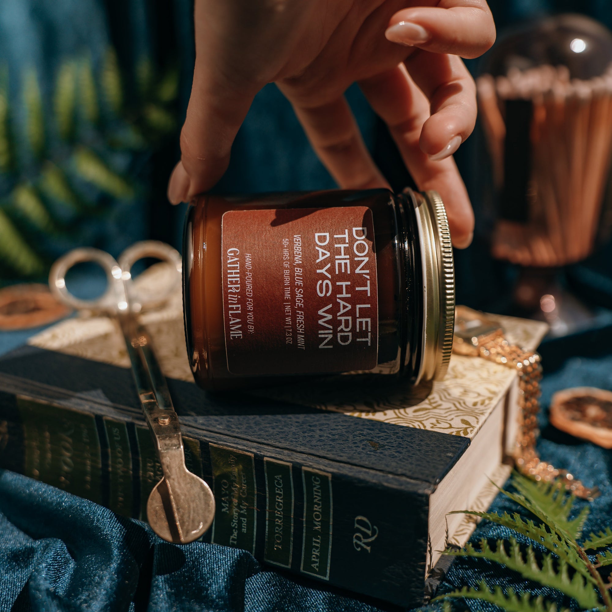Hand holding a candle labeled 'Don't Let the Days Win' over an open book with decorative elements.