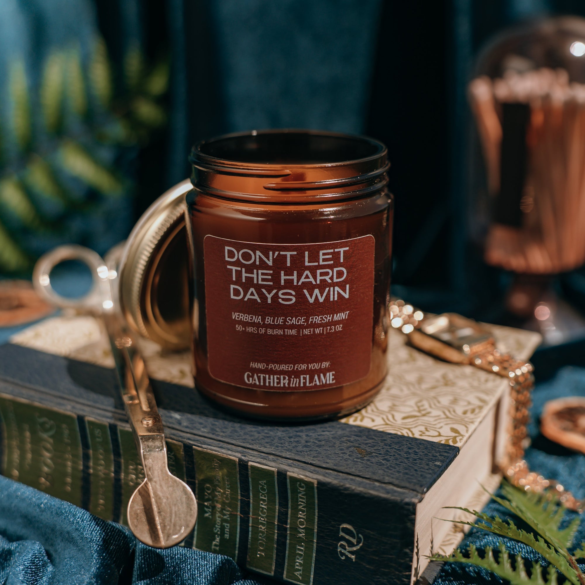Candle jar with text 'Don't let the hard days win' on a reflective surface with decorative elements.