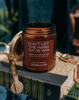 Candle jar with text 'Don't let the hard days win' on a reflective surface with decorative elements.