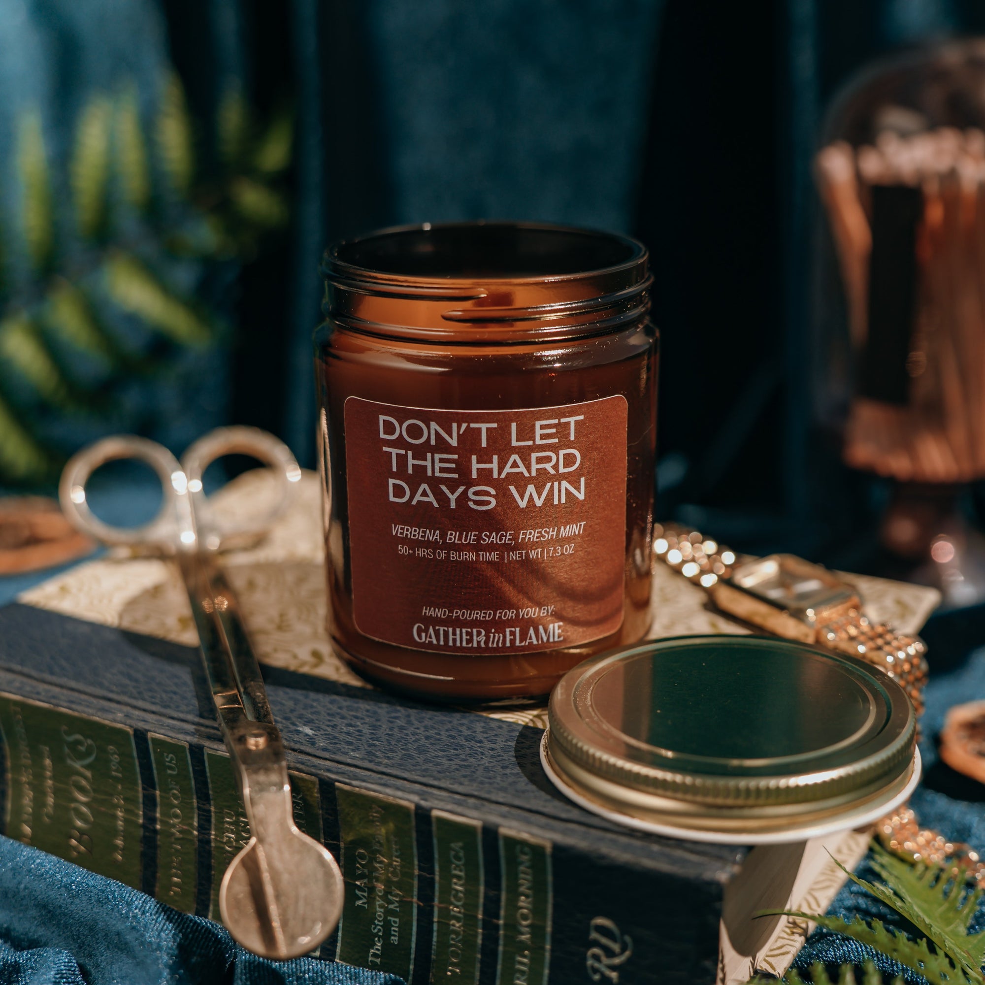 Candle jar with text 'Don't let the hard days win' on a decorative surface with books and scissors.