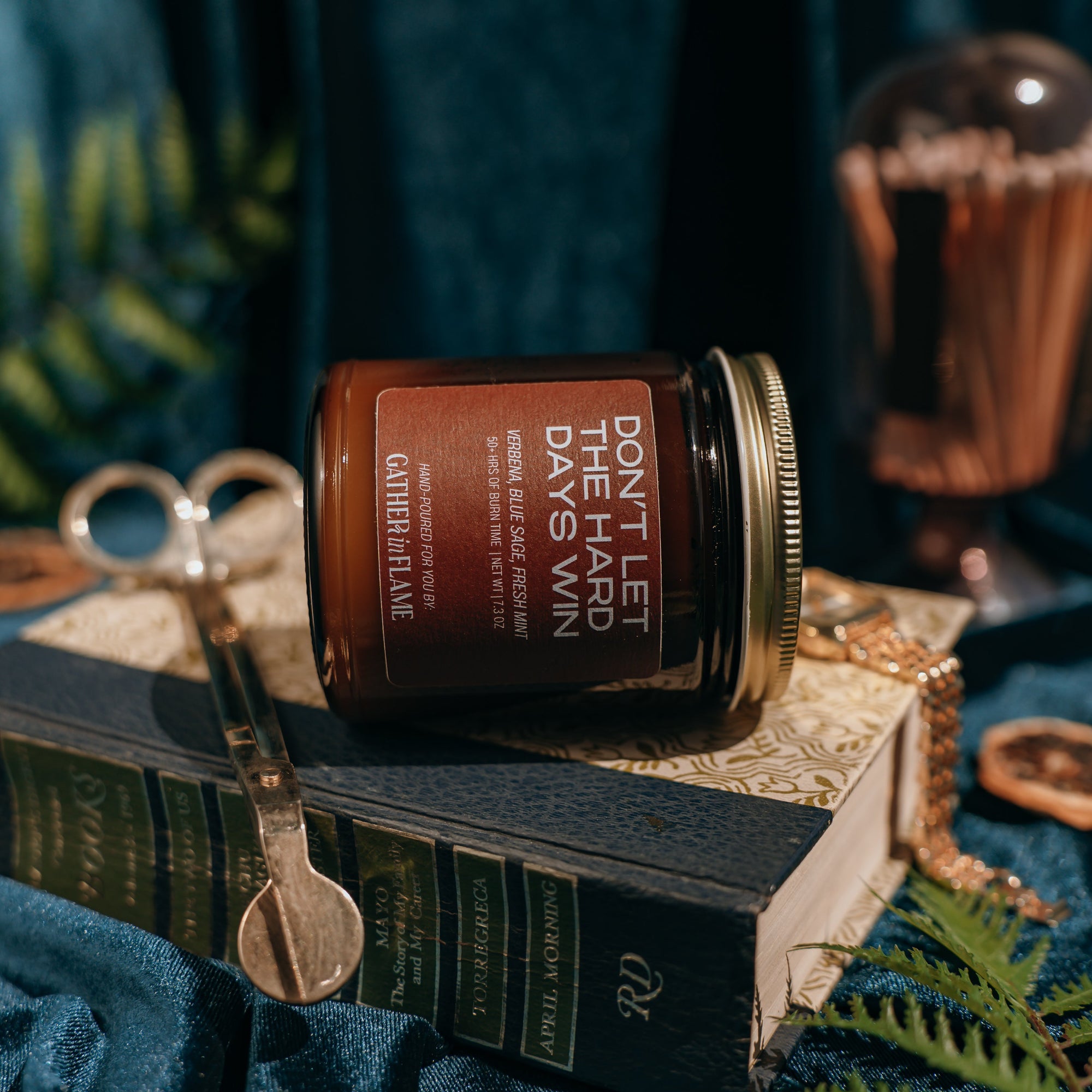 Jar of 'Don't Let the Hard Days Vanish' candle on a book with decorative elements