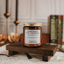Candle labeled 'Enemies to Lovers' on a wooden stand with candles and books in the background.
