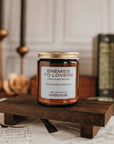 Candle labeled 'Enemies to Lovers' on a wooden stand with candles and books in the background.