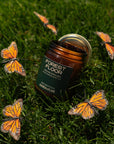 Jar of 'Forest Floor' candle surrounded by monarch butterflies on grass