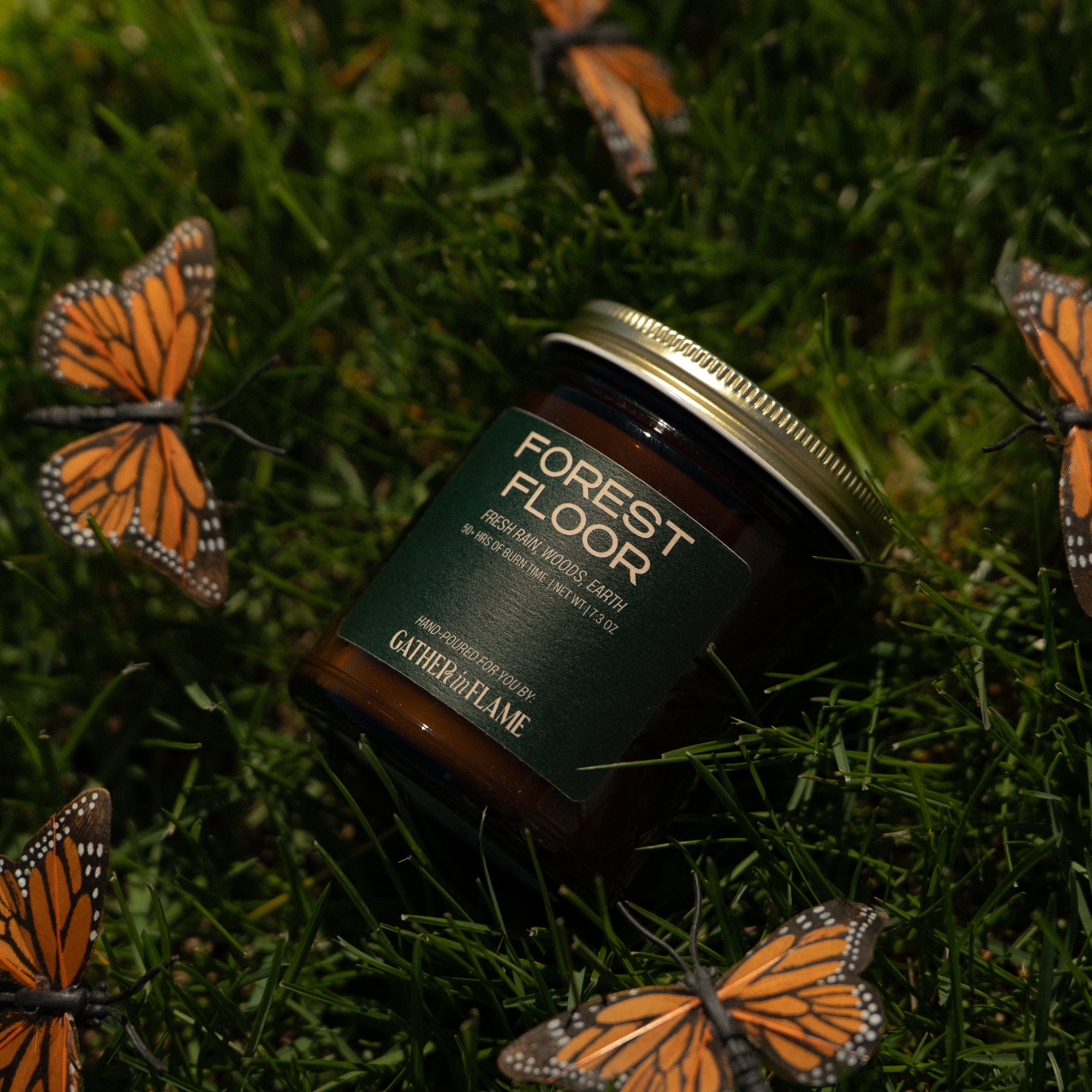 Jar of 'Forest Floor' candle on grass with butterflies