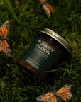 Jar of 'Forest Floor' candle on grass with butterflies