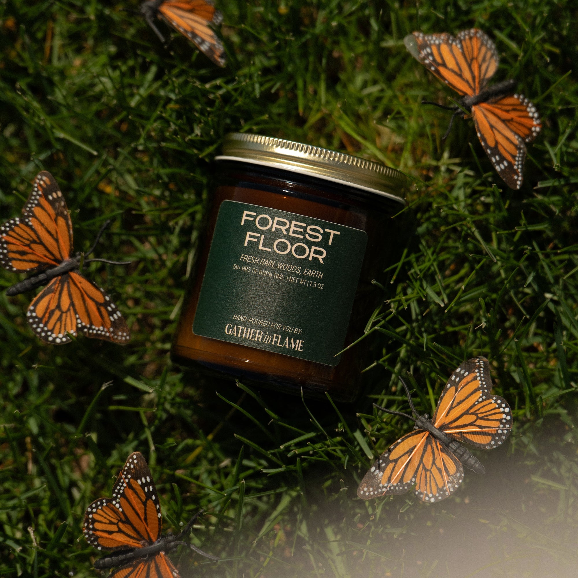 Jar of 'Forest Floor' candle on grass with butterfly decorations