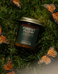 Jar of 'Forest Floor' candle on grass with butterfly decorations