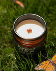 Candle in a container labeled 'Forest Floor' surrounded by butterflies on grass