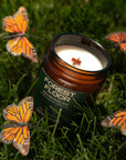 Candle labeled 'Forest Floor' surrounded by butterfly decorations on grass