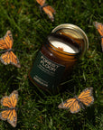 Candle labeled 'Forest Floor' surrounded by monarch butterflies on grass