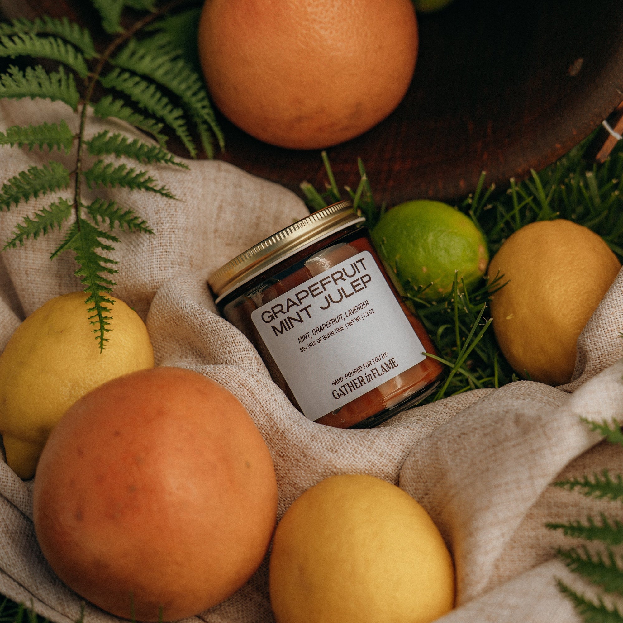 Jar of grapefruit mint julep surrounded by fruits and leaves on a textured surface