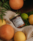 Jar of grapefruit mint julep surrounded by fruits and leaves on a textured surface