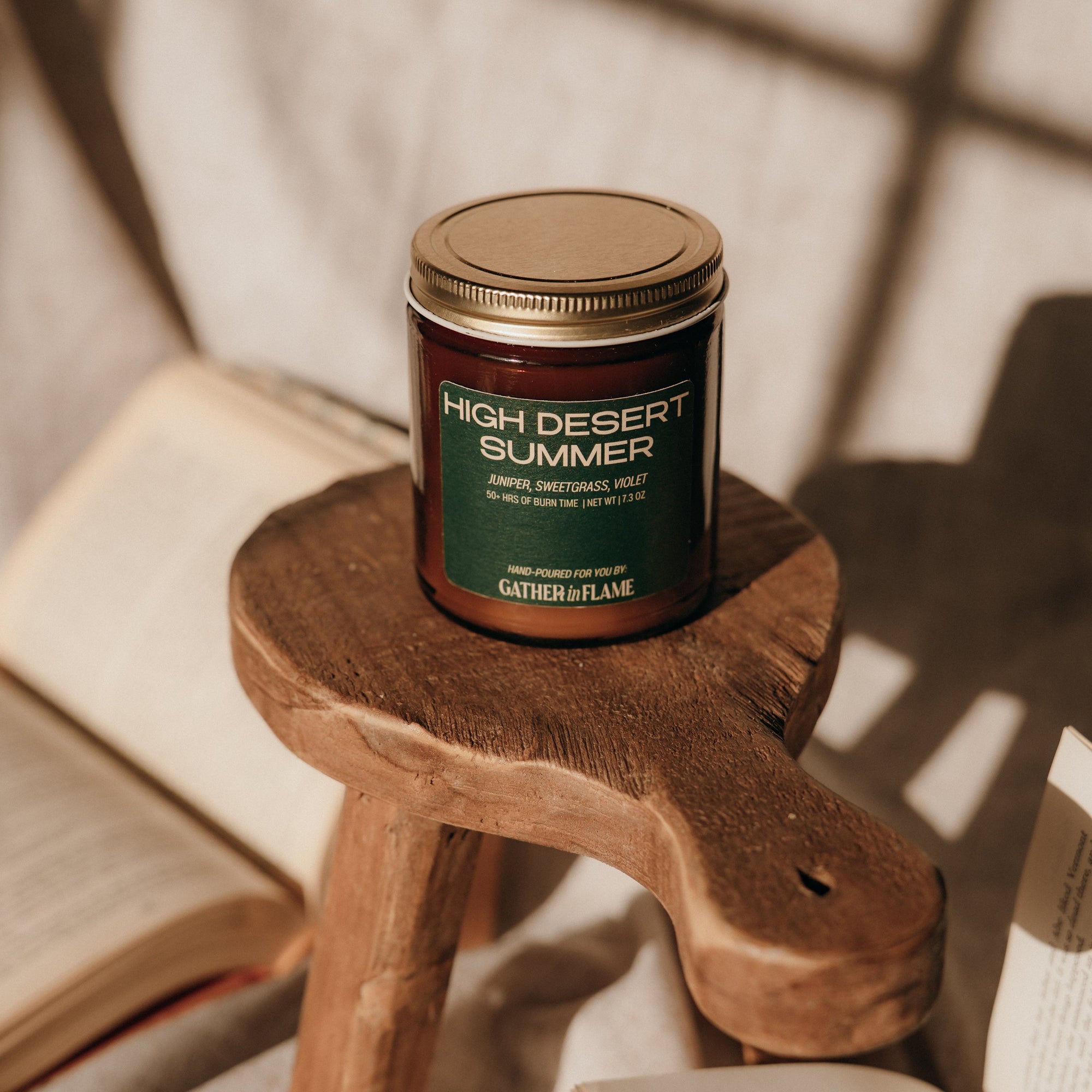 Candle labeled 'High Desert Summer' on a wooden stool with books in the background
