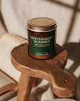 Candle labeled 'High Desert Summer' on a wooden stool with books in the background