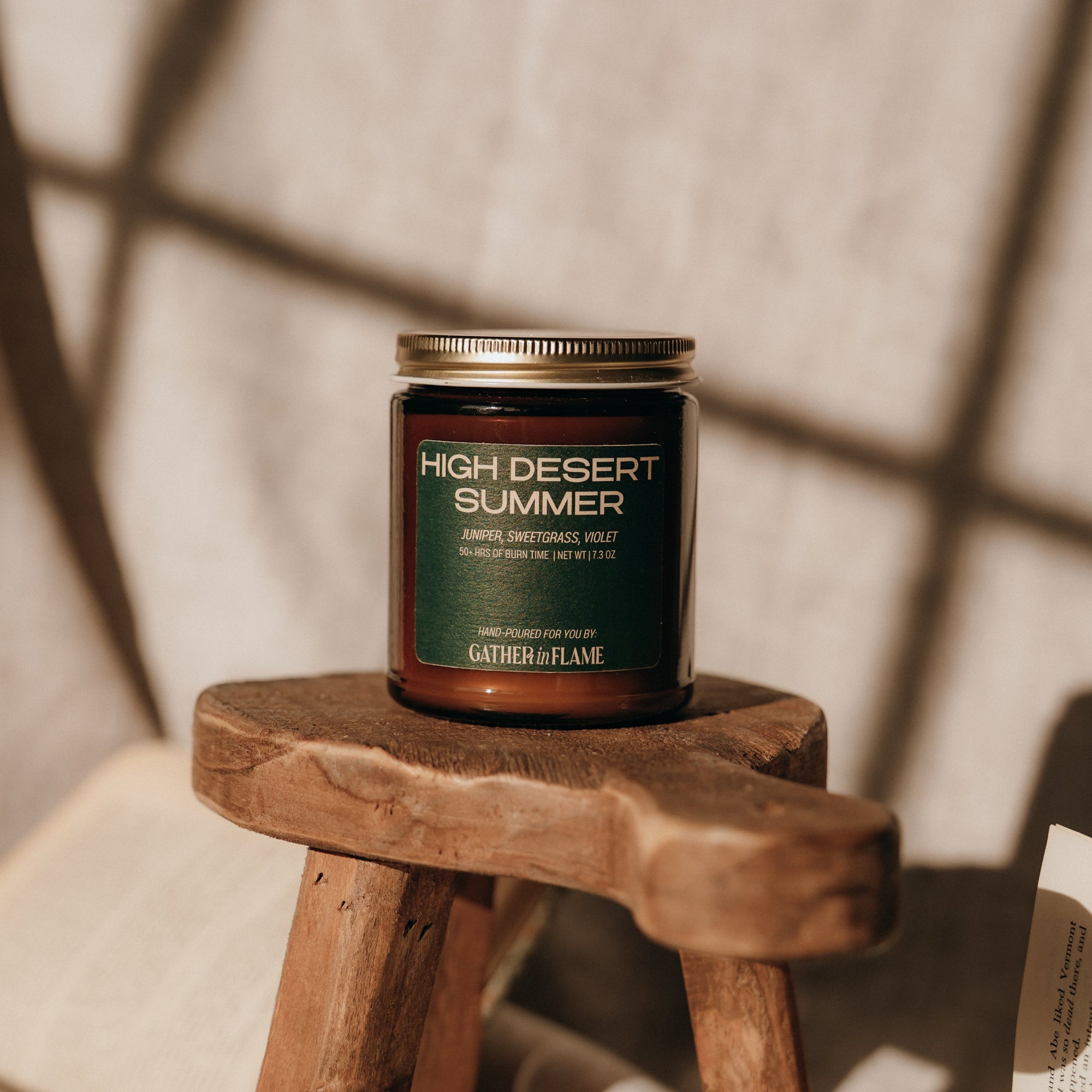 Candle labeled 'High Desert Summer' on a wooden stool with soft lighting