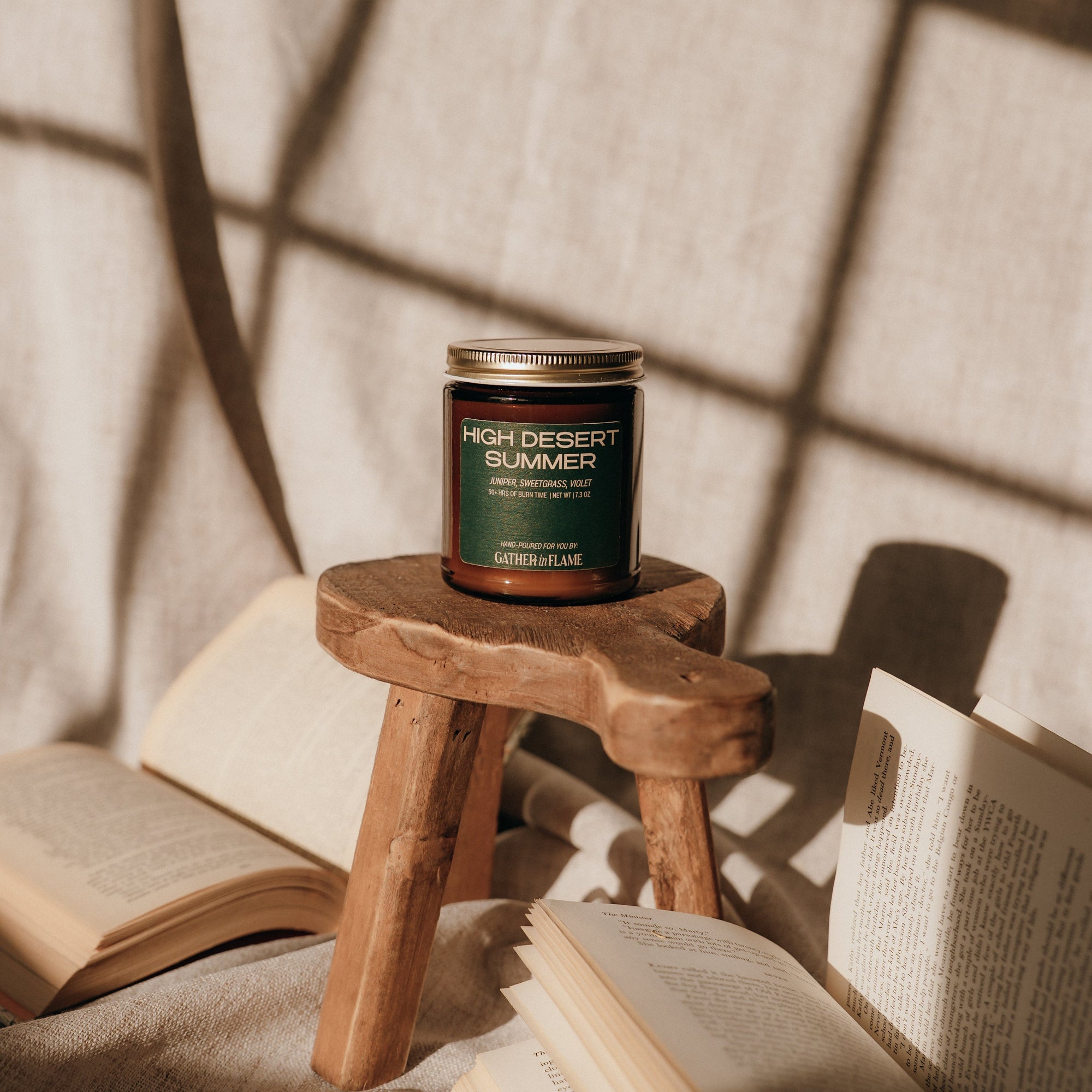 Candle on a wooden stool with open books and a textured wall background