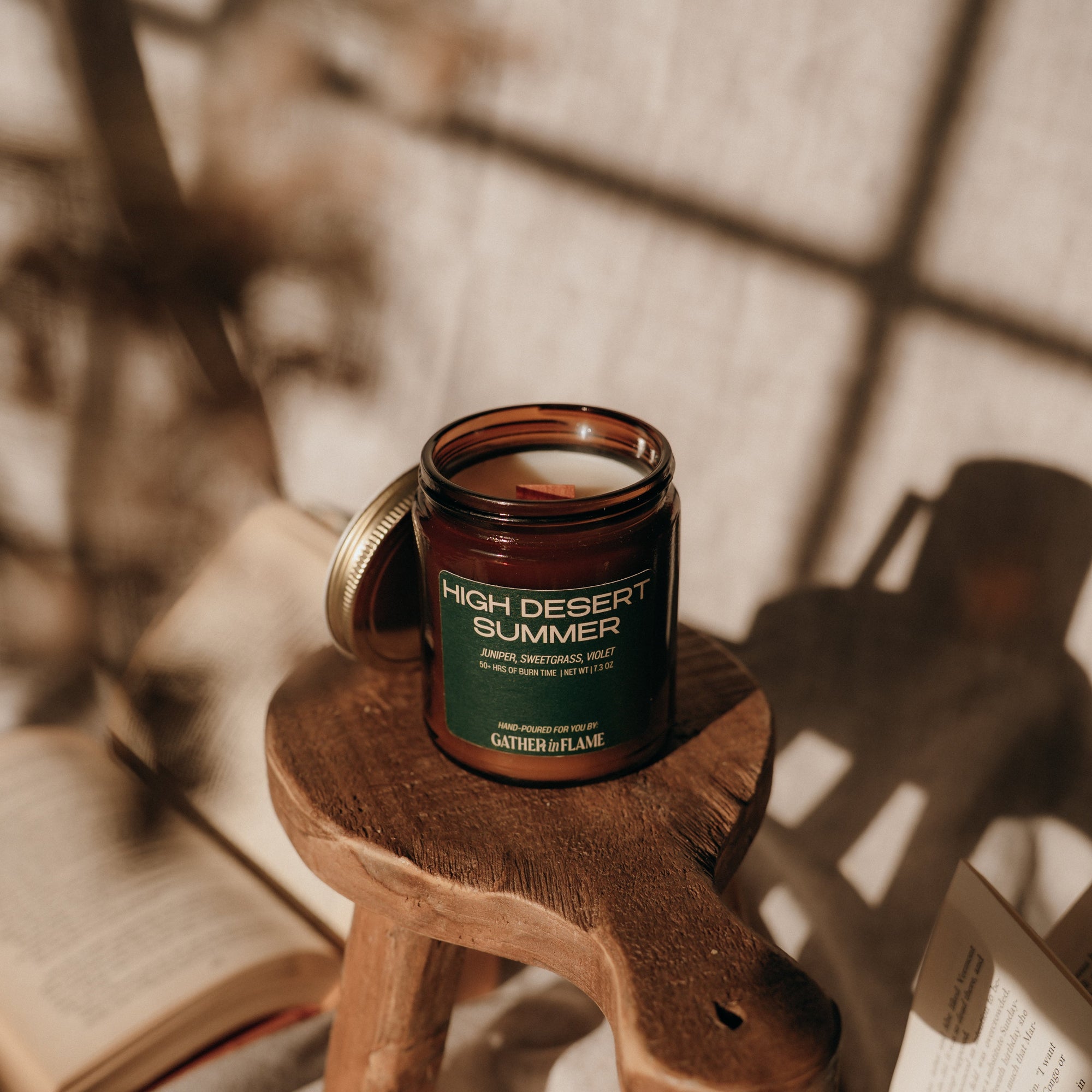 Candle labeled 'High Desert Summer' on a wooden stool with books in the background