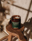 Candle labeled 'High Desert Summer' on a wooden stool with books in the background