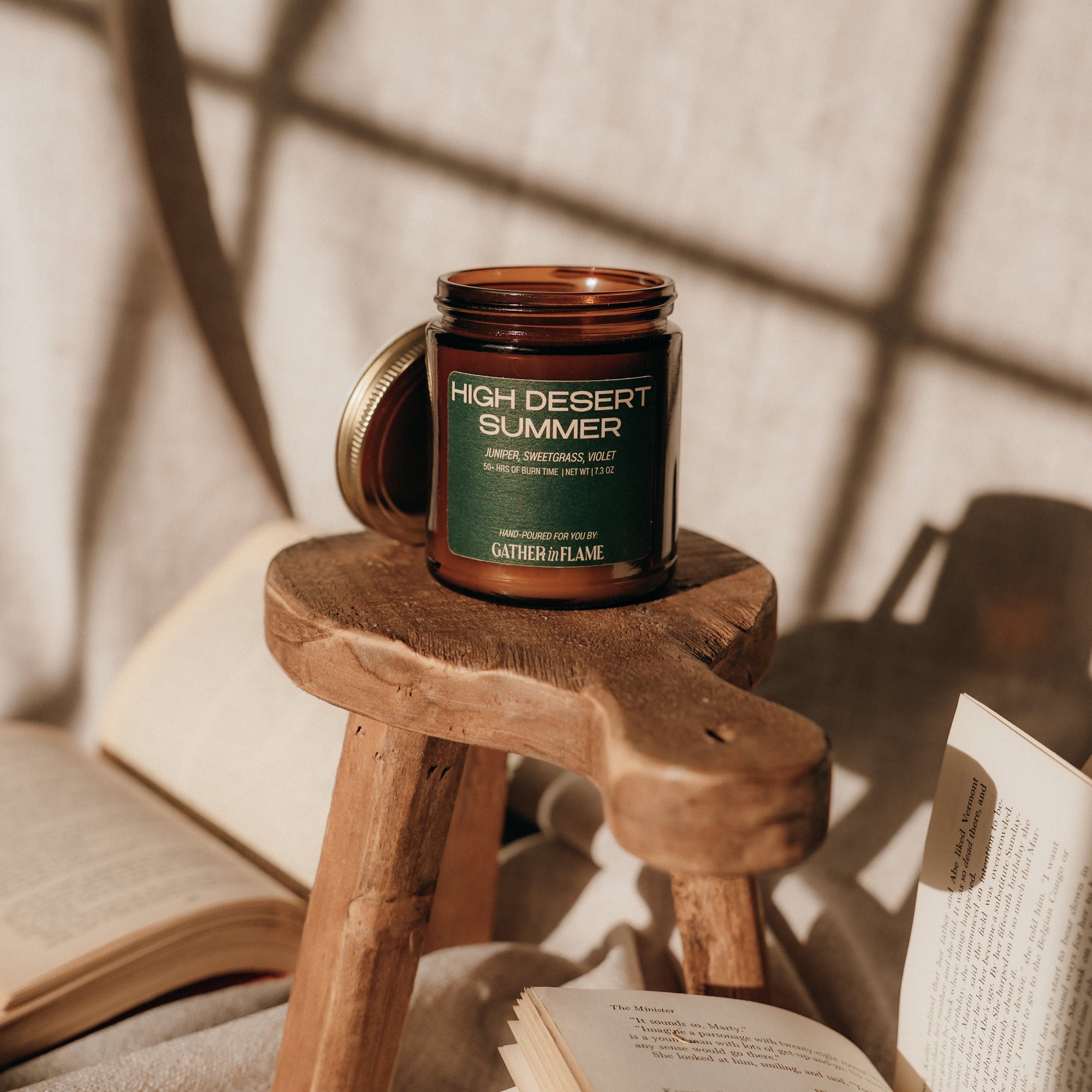 Candle labeled 'High Desert Summer' on a wooden stool with books in the background