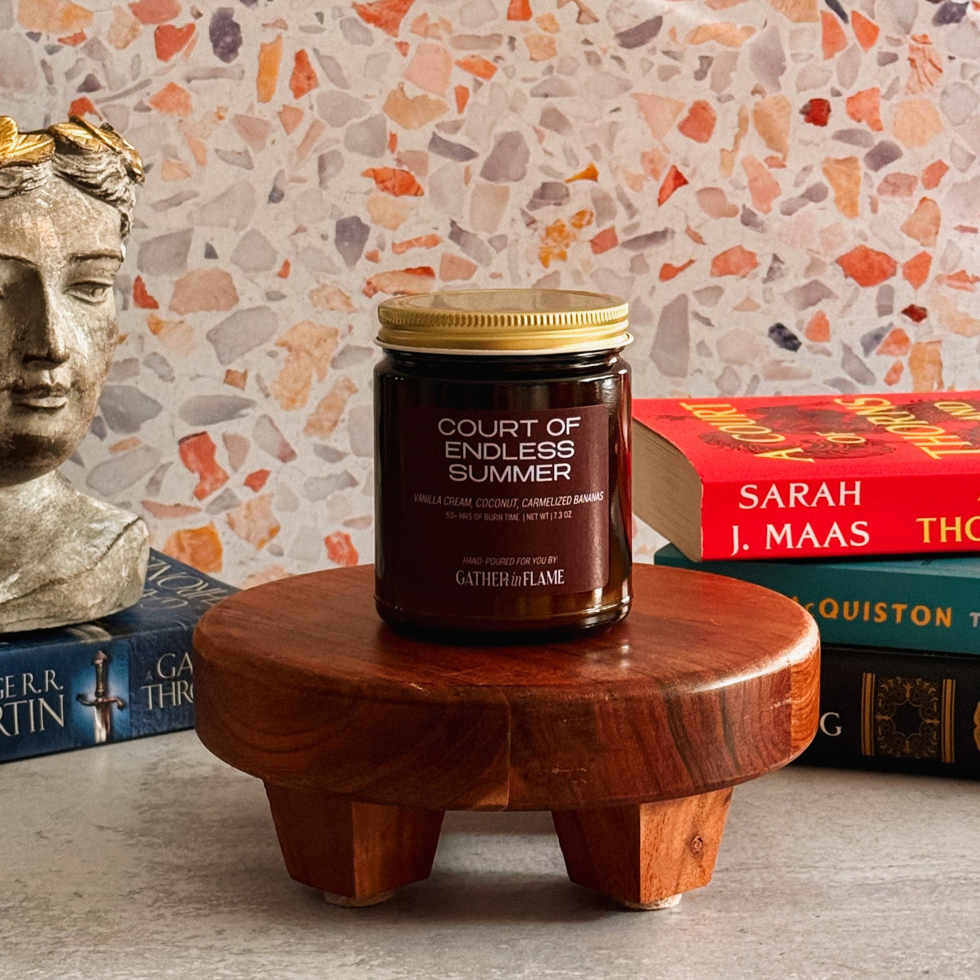 Candle on a wooden stand with books and a decorative wall in the background