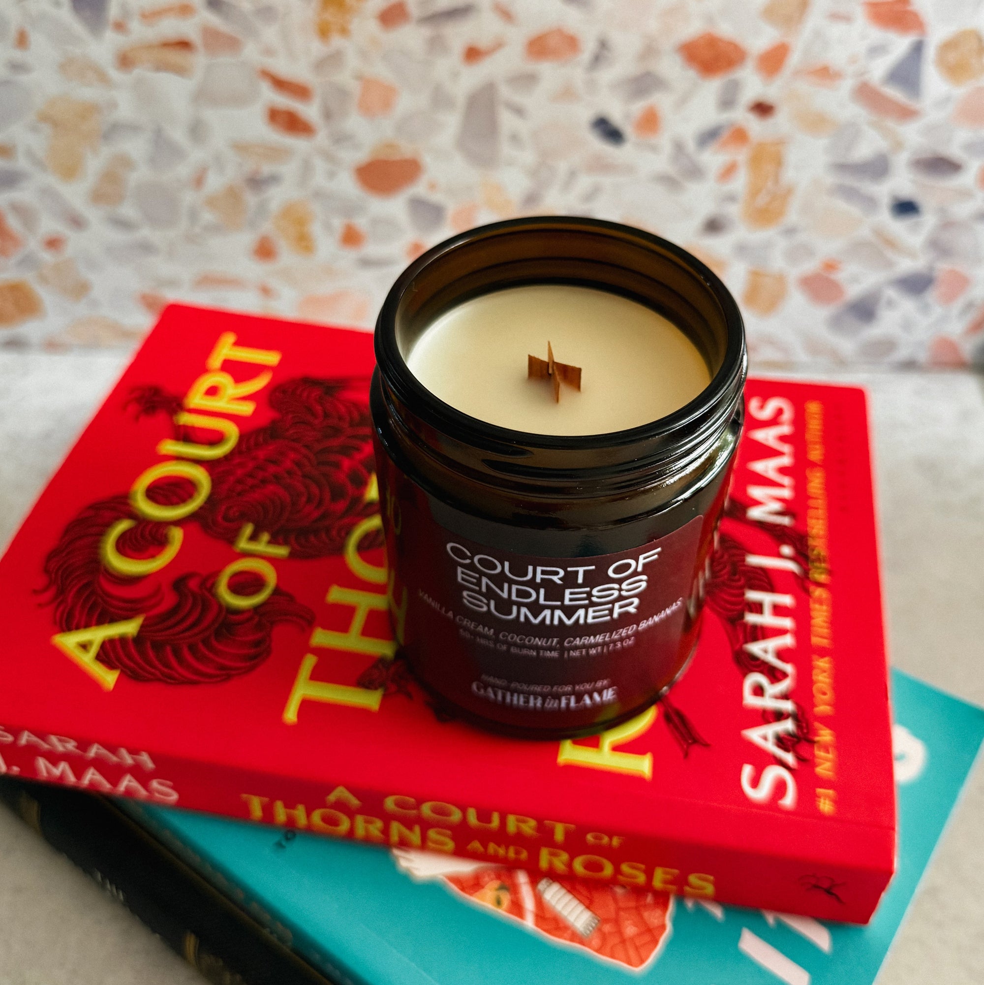 Candle in a 'Court of Thorns and Roses' book-themed container on top of books with a colorful background.