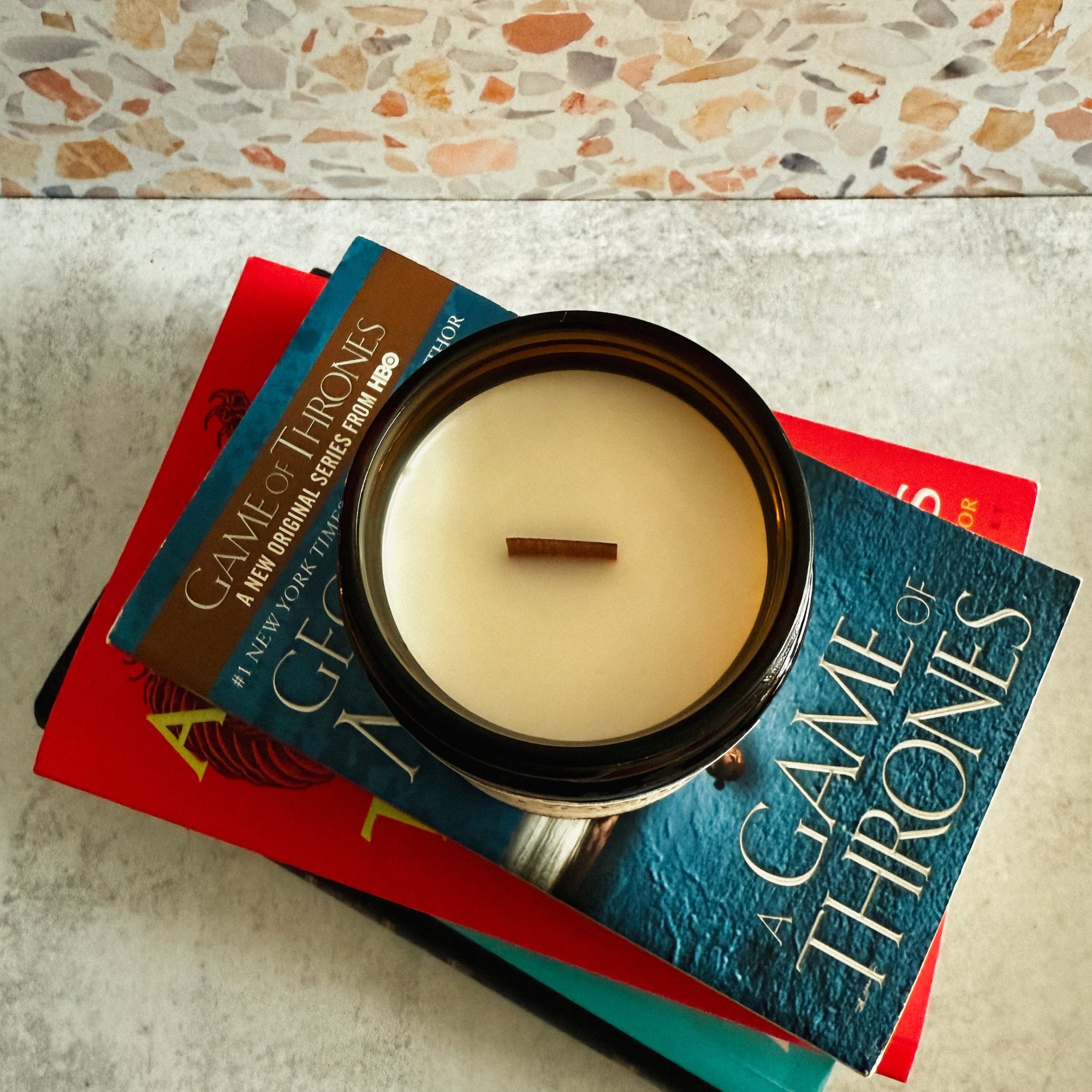 Candle in a holder on top of 'A Game of Thrones' books with a textured wall background