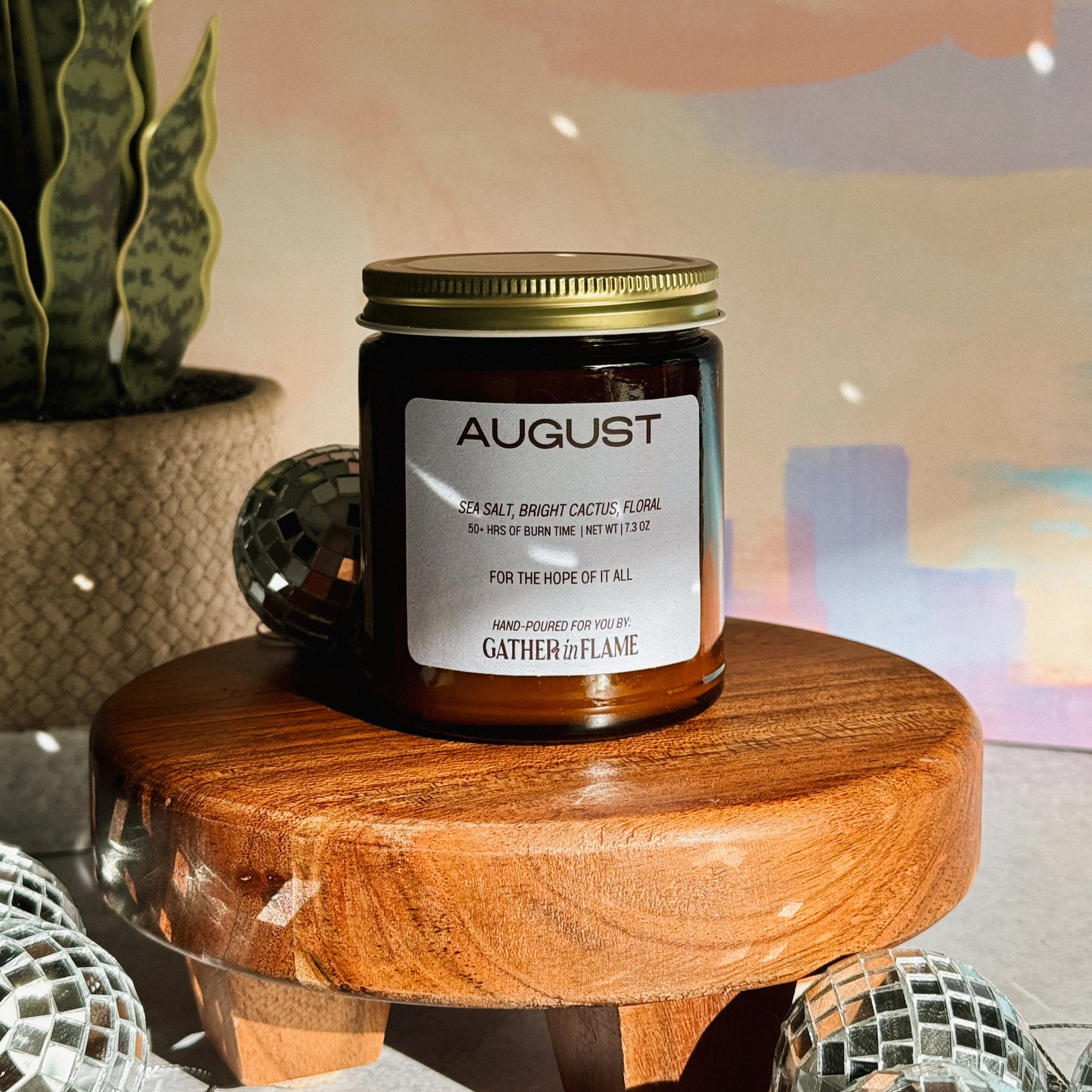 Candle jar labeled 'August' on a wooden stool with a blurred background