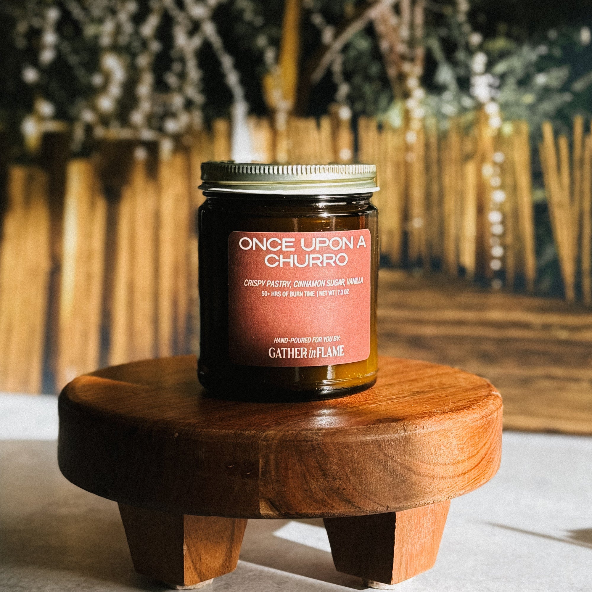Jar of 'Once Upon a Churro' candle on a wooden stand with a blurred natural background
