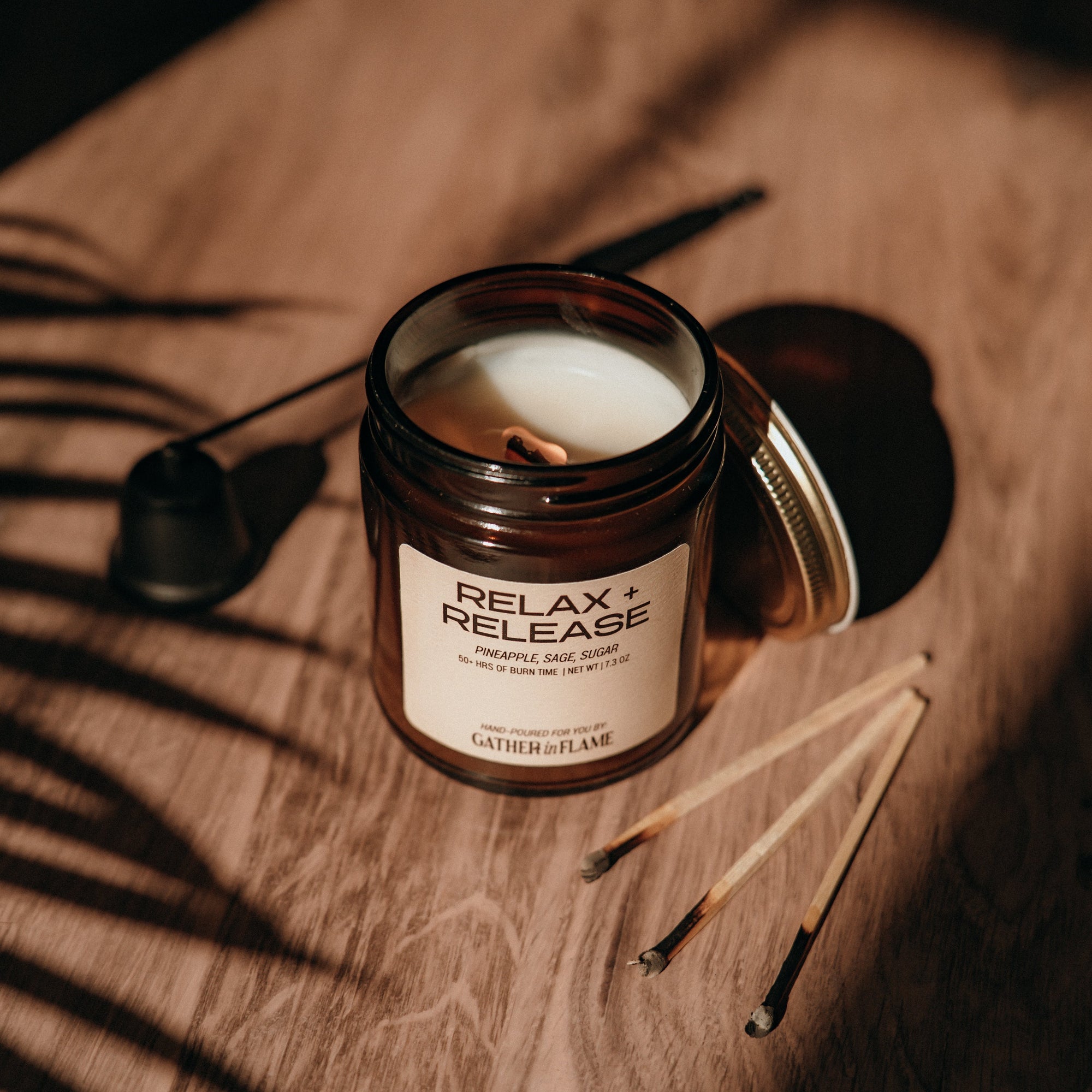 Candle in a glass jar labeled 'Relax &amp; Release' on a wooden surface with shadows.