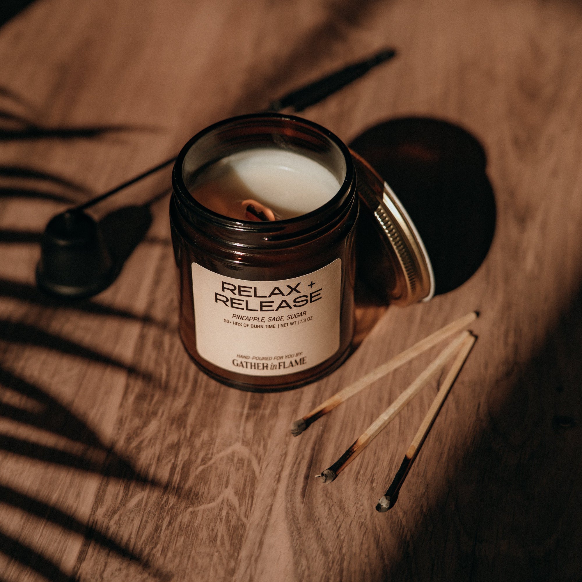 Candle labeled 'Relax + Release' on a wooden surface with shadows cast by leaves.