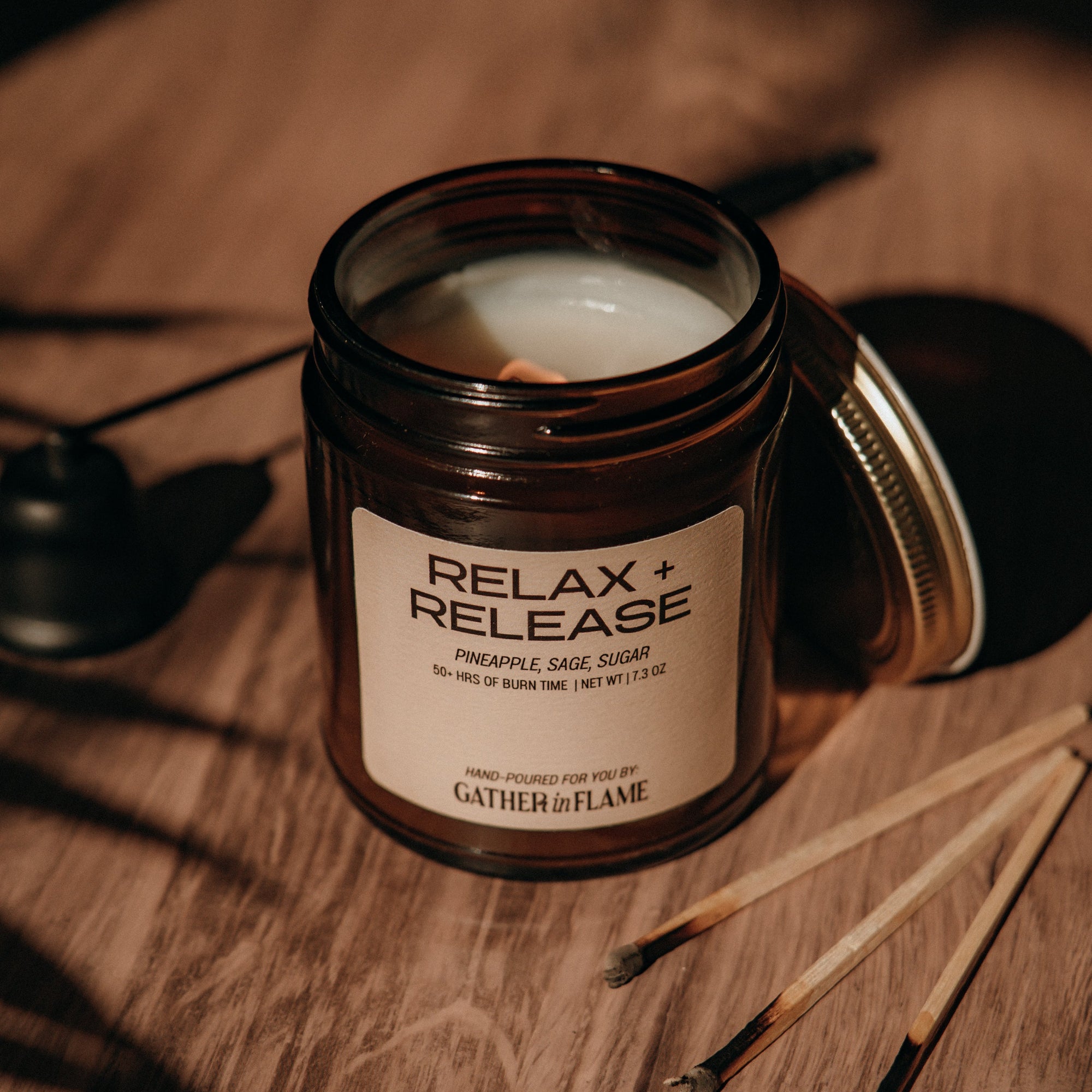 Candle in a glass jar labeled 'Relax Release' on a wooden surface with matches.
