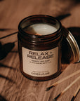 Candle in a glass jar labeled 'Relax Release' on a wooden surface with matches.