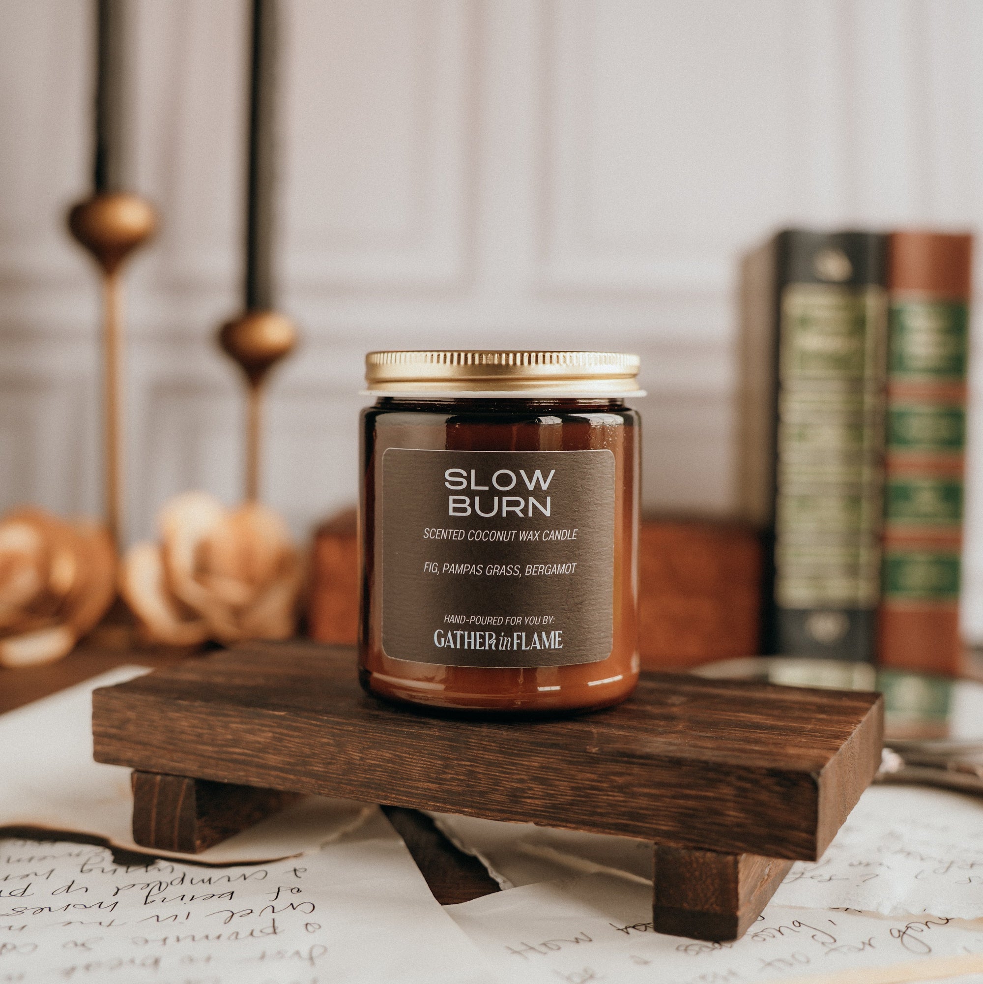 Candle jar labeled 'Slow Burn' on a wooden stand with books and candles in the background.