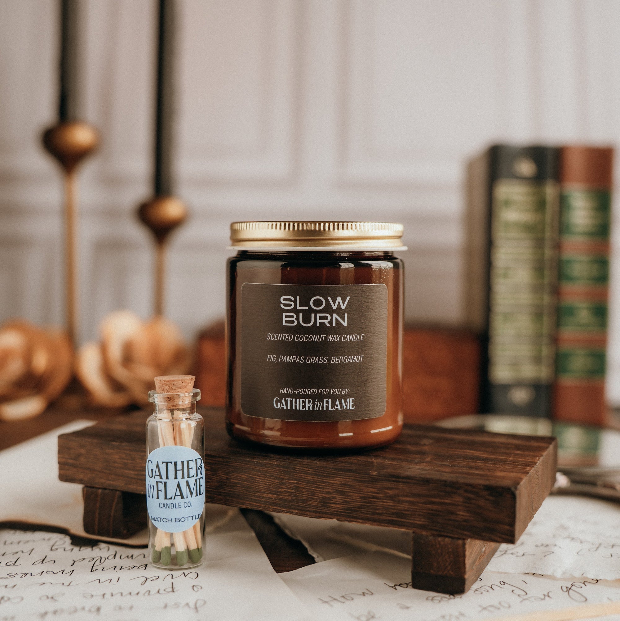 Candle with 'Slow Burn' label on a wooden stand, surrounded by books and candles.